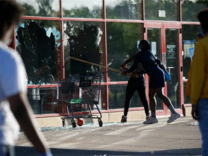 A man breaks a window at a tire store Thursday, May 28, 2020, in St. Paul, Minn. Minnesota Gov. Tim Walz called in the National Guard on Thursday as looting broke out in St. Paul and a wounded Minneapolis braced for more violence after rioting over the death of George …