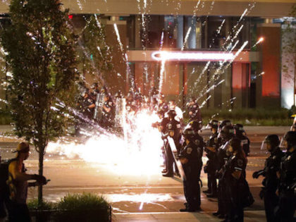 A firework explodes by a police line as demonstrators gather to protest the death of Georg