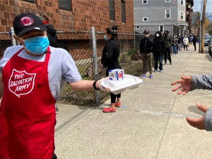A Salvation Army worker, left, wears a mask out of concern about the coronavirus while handing out a lunch box as people form a line along a sidewalk in front of a Salvation Army food pantry, Tuesday, April 21, 2020, in Chelsea, Mass. (AP Photo/Rodrique Ngowi)