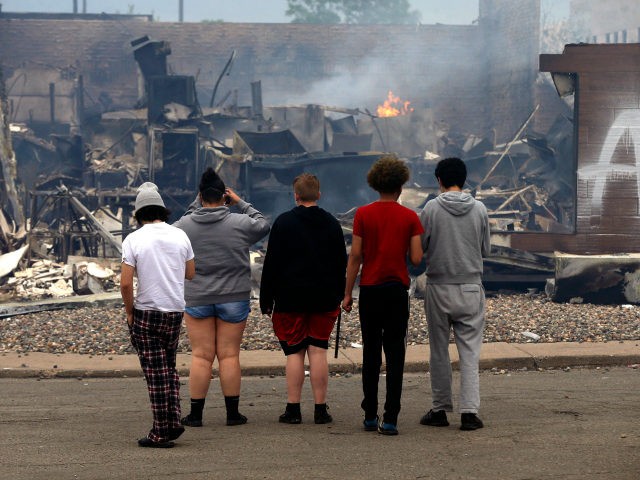 Onlookers watch as smoke smolders from a destroyed fast food restaurant near the Minneapolis Police Third Precinct, Thursday, May 28, 2020, after a night of rioting and looting as protests continue over the death of George Floyd, who died in police custody Monday night in Minneapolis after video shared online …