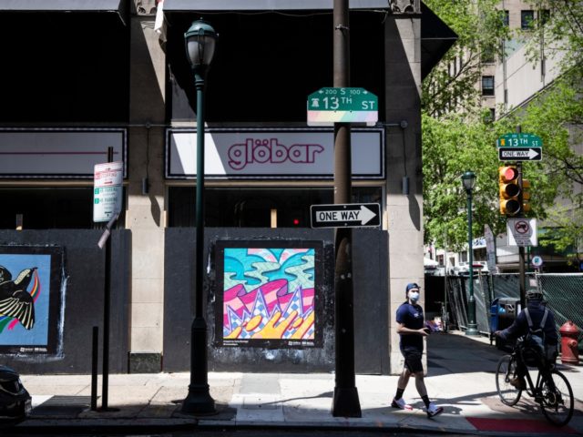People pass newly installed posters on a shuttered businesses in Philadelphia, Monday, May