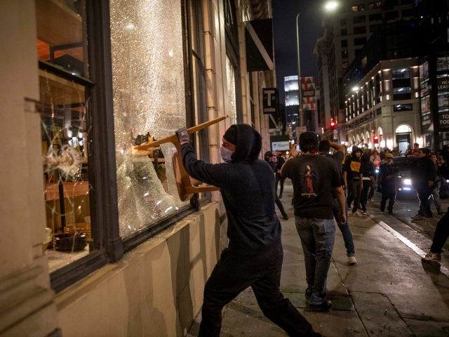 A protester breaks a window with a chair during a protest in downtown Los Angeles, Friday,