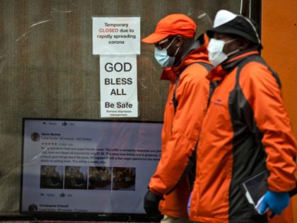 Pedestrians in protective face mask walk past a closed business in Philadelphia, Friday, M