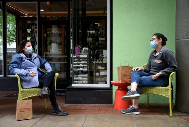 Friends wearing face masks chat in front of a shop during the outbreak of COVID-19 in Arlington, Virginia © AFP/File Olivier DOULIERY