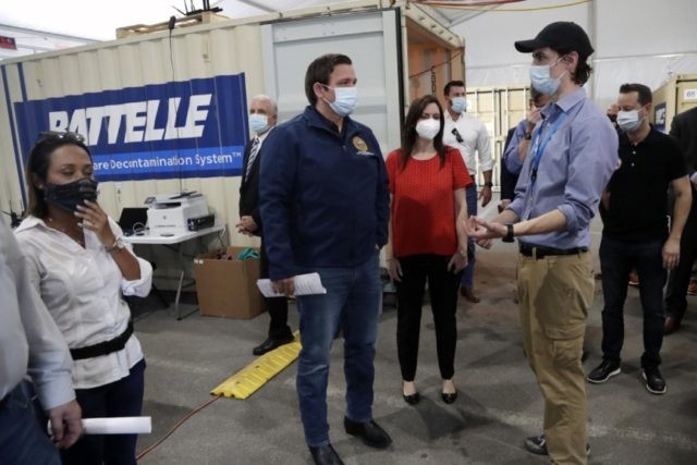 In this Wednesday, May 6, 2020 file photo, Gov. Ron DeSantis, center, tours decontamination units at a COVID-19 testing site with Sean Harrington, of Battelle Critical Care Decontamination System, right, at Hard Rock Stadium, during the new coronavirus pandemic in Miami Gardens, Fla. Battelle decontaminates N95 masks used by health …