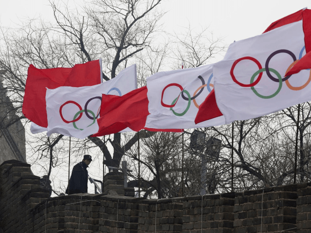A security person stands near the Olympic flags during a ceremony to mark the arrival of the Olympic flag and start of the flag tour for the Winter Olympic Games Beijing 2022 at a section of the Great Wall of China in Beijing Tuesday, Feb. 27, 2018. (AP Photo/Ng Han …