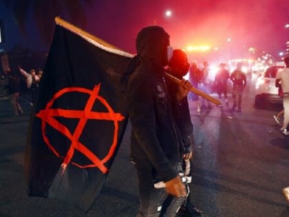 A man carries a flag depicting the anarchist symbol during a public disturbance on Melrose