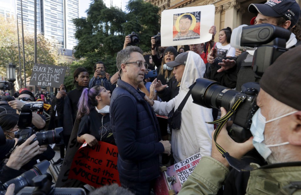 A man who appears to be a counter protester, center, is pushed away after briefly takes the stage carrying a sign saying, "White Lives, Black Lives, All Lives Matter" before police removes him as protesters gather in Sydney, Saturday, June 6, 2020, to support the cause of U.S. protests over the death of George Floyd. Black Lives Matter protests across Australia proceeded mostly peacefully as thousands of demonstrators in state capitals honored the memory of George Floyd and protested the deaths of indigenous Australians in custody. (AP Photo/Rick Rycroft)