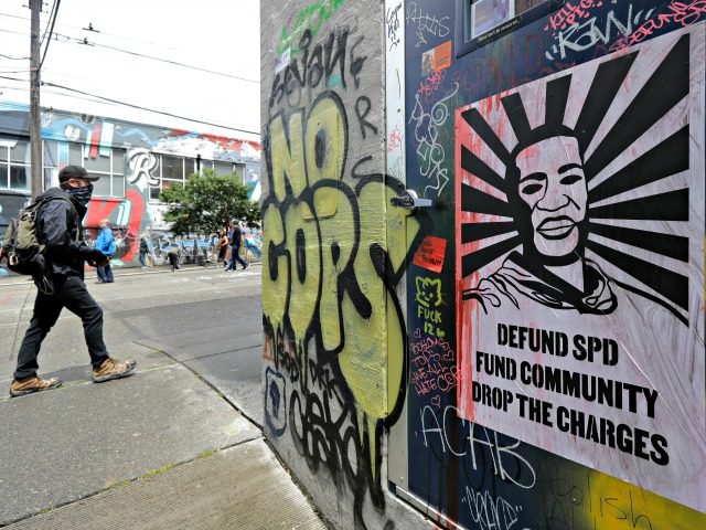 A person walks past an image of George Floyd in an alleyway, Thursday, June 11, 2020, inside what is being called the "Capitol Hill Autonomous Zone" in Seattle. Following days of violent confrontations with protesters, police in Seattle have largely withdrawn from the neighborhood, and protesters have created a festival-like …