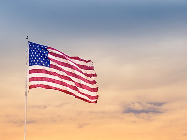 American flag blowing in the wind against beautiful sunset.