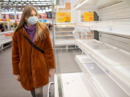 Young woman in medical mask and empty shelves in supermarket