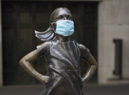 Fearless Girl, a bronze sculpture by Kristen Visbalthe, with a PPE mask on in front of the