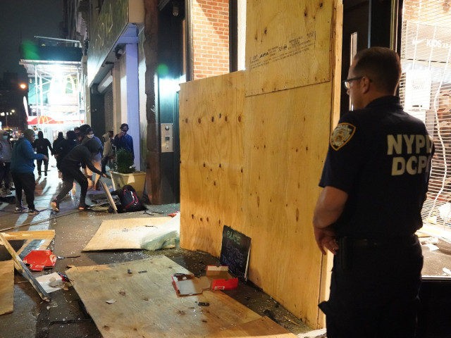 People loot a store as a NYPD police officer waches during demonstrations over the death o
