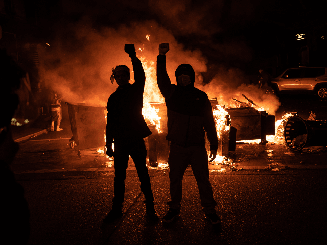 Demonstrators raise their fists as a fire burns in the street after clashes with law enfor
