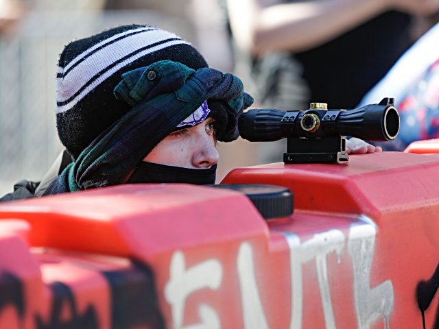 A protester uses a scope on top of a barricade to look for police approaching the newly created Capitol Hill Autonomous Zone (CHAZ) in Seattle, Washington on June 11, 2020. - The area surrounding the East Precinct building has come to be known as the CHAZ, Capitol Hill Autonomous Zone. …