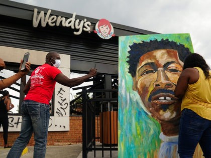TOPSHOT - People use their cellphones to document a muralist painting the face of Rayshard Jones outside a burned Wendys restaurant on the second day following his shooting death by police in the restaurant parking lot June 14, 2020, in Atlanta, Georgia. - The fatal shooting of a black man …