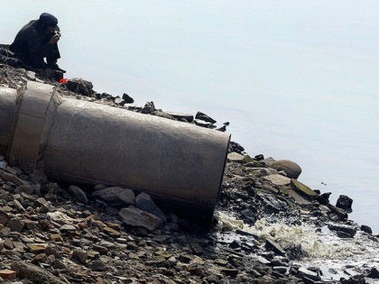 LANZHOU, CHINA: A man sits by the banks of the Yellow River beside a sewage pipe emitting
