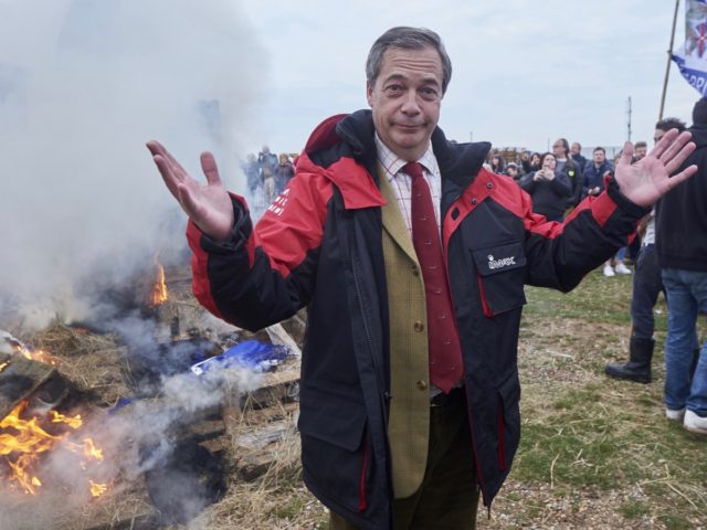 Former UK Indepence Party (UKIP) Leader Nigel Farage (C) stands beside the remains of a small boat on top of a bonfire on the shore during a demonstration in Whitstable, southeast England on April 8, 2018 against the Brexit transition deal that would see Britain continue to adhere to the …