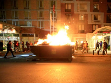 People walk past a dumpster fire in front of the Hampton Inn on west 35th street during a