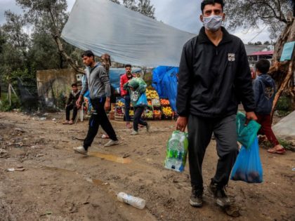 TOPSHOT - Migrants and refugees carry bags with food at a makeshift camp next to the Moria camp on the Greek island of Lesbos on April 2, 2020. - Over 20 coronavirus cases were found in a camp near Athens this week. At the camp of Moria on the island …