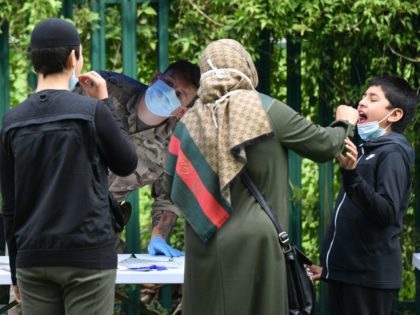 A member of the armed forces watches as members of a family administer a self-test at a st
