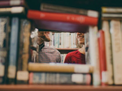 Man and woman's partial faces as they are seen smiling through books at a library.