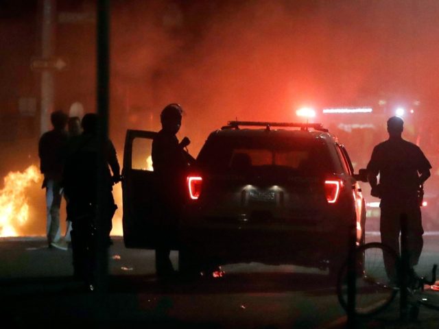 A police car burns, left rear, after being set on fire in Boston, Sunday, May 31, 2020, fo