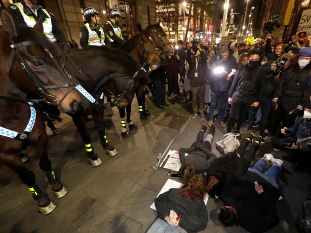 Protesters lay on the ground in front of police on horseback as they gather in Sydney, Tue