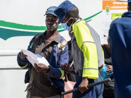 A police officer inspects permits belonging to passengers boarding onto a city bound commuter bus at a check point on April 20, 2020, in Emakhandeni township, Bulawayo, Zimbabwe. - Roadblocks have been intensified to reduce the number of motorists and passengers entering the Central Business District since Zimbabwe President Emmerson …