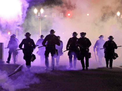 In this March 29, 2020, file photo, police officers walk enveloped by tear gas in Portland