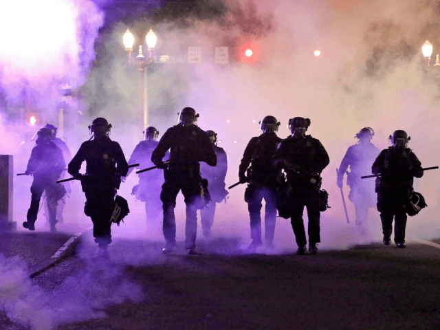 In this March 29, 2020, file photo, police officers walk enveloped by tear gas in Portland, Ore. City commissioners in Portland voted Wednesday, June 17, 2020 to cut nearly $16 million from the Portland Police Bureau's budget in response to concerns about police brutality and racial injustice. The cuts are …