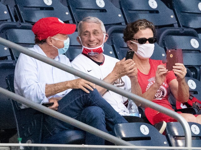 Dr. Anthony Fauci, director of the National Institute of Allergy and Infectious Diseases, center, smiles as he watches an opening day baseball game between the Washington Nationals and the New York Yankees at Nationals Park, Thursday, July 23, 2020, in Washington. (AP Photo/Alex Brandon)