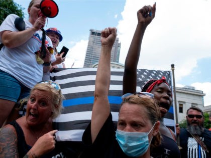 Black Lives Matter protestors raise their fists in front of a "Blue Lives Matter" flag during an anti-mask right-wing protest "Stand For America Against Terrorists and Tyrants" at State Capitol on July 18, 2020 in Columbus, Ohio. - Protestors descended on Columbus, Ohio for a planned anti-mask rally in response …