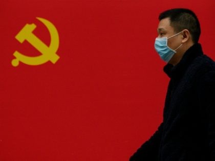 A man wearing a face mask as a preventive measure against the COVID-19 coronavirus walks past a Communist Party flag along a street in Wuhan in China's central Hubei province on March 31, 2020. (Photo by NOEL CELIS / AFP) (Photo by NOEL CELIS/AFP via Getty Images)