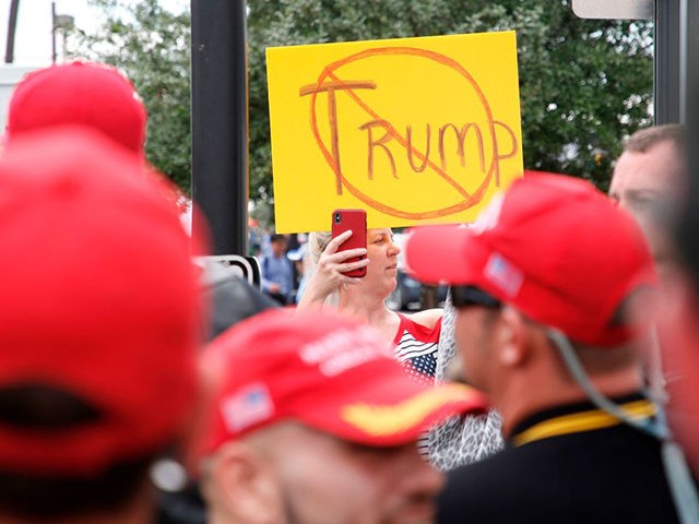 An anti-Trump demonstrator holds up a placard and films a group of supporters of US President Donald Trump, wearing "Make America Great Again" hats, near the Amway Center on June 18, 2019, Orlando, Florida. - President Trump is expected to launch his 2020 re-election campaign in Orlando, June 18. (Photo …