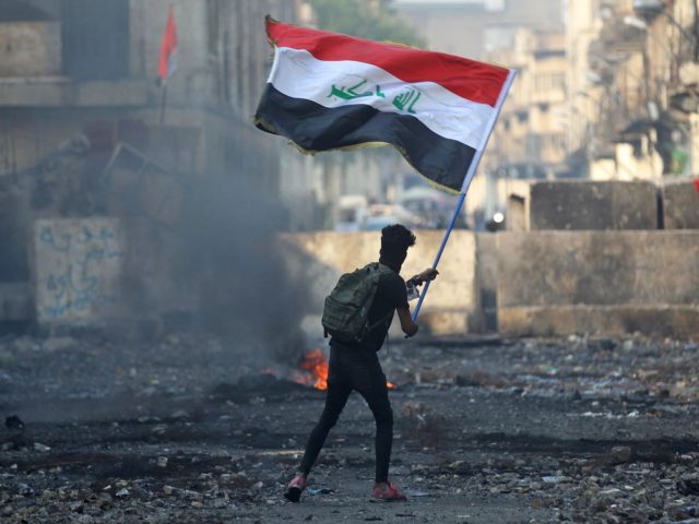 An Iraqi anti-government protester waves a national flag close to a concrete barricade ami