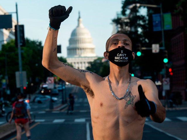 A Black Lives Matter protester wearing a "I Can't Breate" mask raises his fist during a de