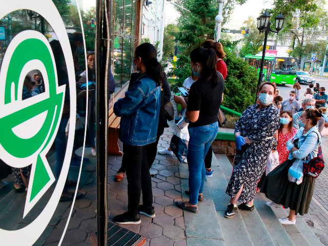 People wearing face masks stand in a line outside a pharmacy in Almaty on June 29, 2020. -