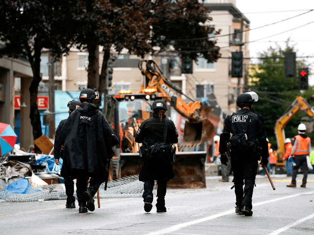 Seattle Police walk past debris and bulldozing equipment outside the Seattle Police Depart