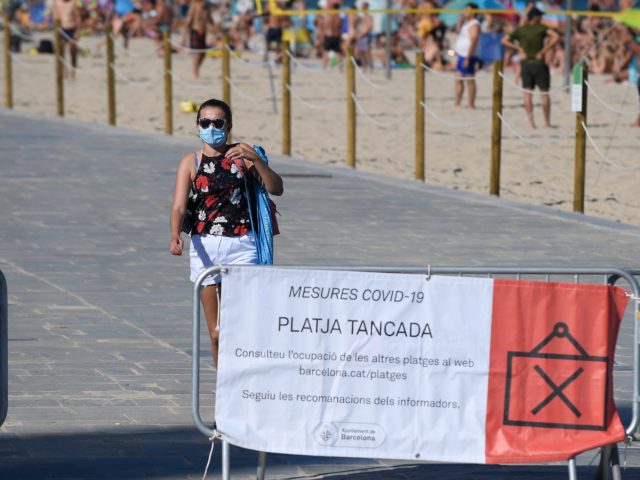 A woman leaves the beach as a sign on a fence informs people of the closure of the beach d