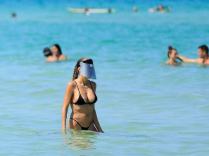 MIAMI BEACH, FLORIDA - JUNE 10: A woman wears a face shield as she wades in the ocean off