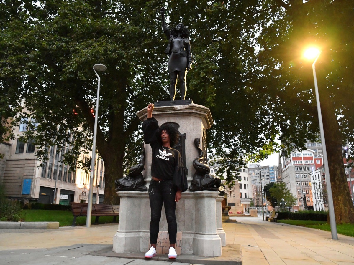 BRISTOL, ENGLAND - JULY 15: Black Lives Matter protestor Jen Reid poses for a photograph in front of a sculpture of herself, by local artist Marc Quinn, on the plinth where the Edward Colston statue used to stand on July 15, 2020 in Bristol, England. A statue of slave trader Edward Colston was pulled down and thrown into Bristol Harbour during Black Lives Matter protests sparked by the death of an African American man, George Floyd, while in the custody of Minneapolis police in the United States of America. The Mayor of Bristol has since announced the setting up of a commission of historians and academics to reassess Bristol's landmarks and buildings that feature the name of Colston and others who made fortunes in trades linked to slavery. (Photo by Matthew Horwood/Getty Images)