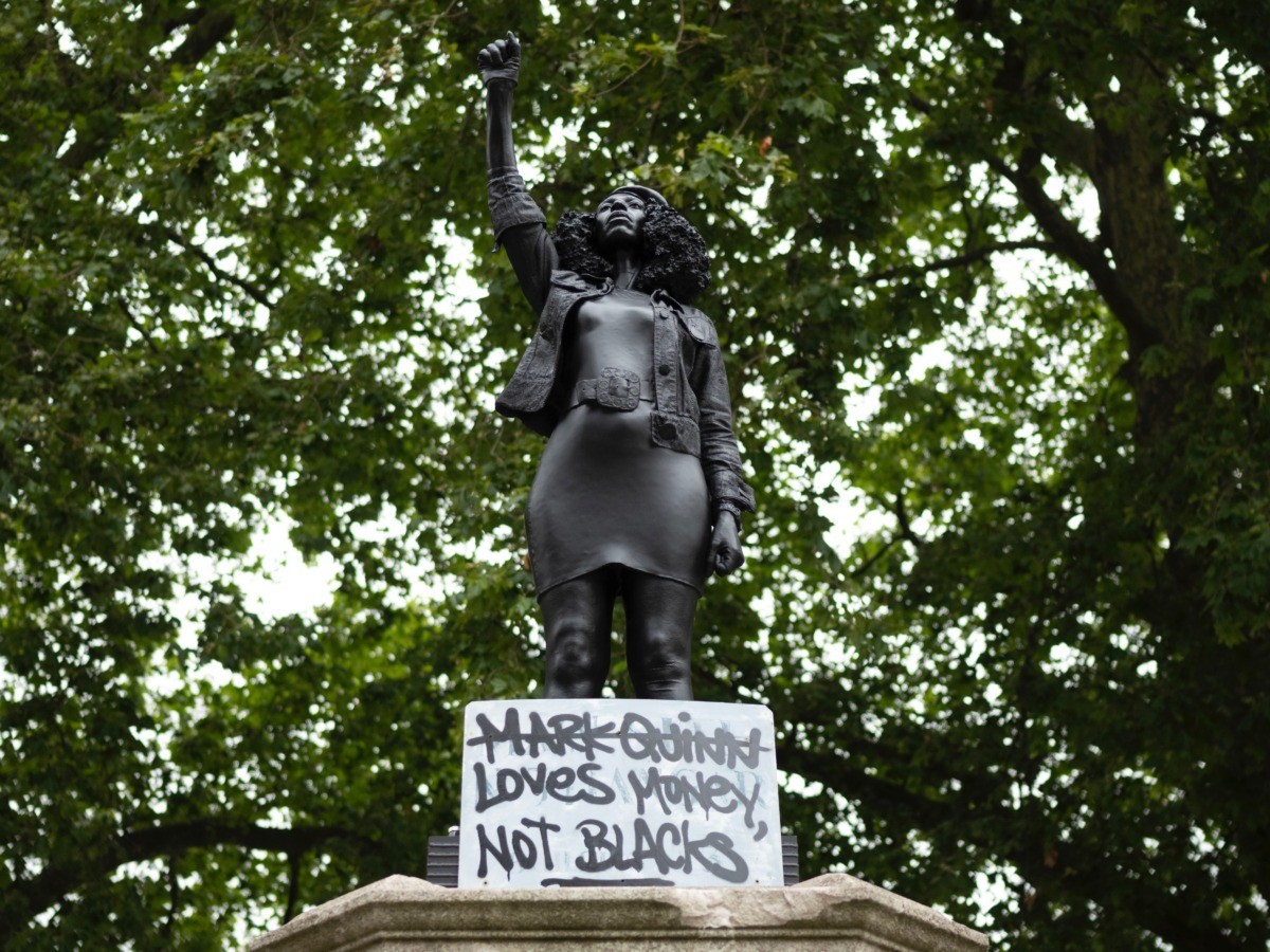 BRISTOL, ENGLAND - JULY 15: A sign saying "Marc Quinn loves money not blacks" is placed on a new sculpture, by local artist Marc Quinn, of Black Lives Matter protestor Jen Reid on the plinth where the Edward Colston statue used to stand on July 15, 2020 in Bristol, England. A statue of slave trader Edward Colston was pulled down and thrown into Bristol Harbour during Black Lives Matter protests sparked by the death of an African American man, George Floyd, while in the custody of Minneapolis police in the United States of America. The Mayor of Bristol has since announced the setting up of a commission of historians and academics to reassess Bristol's landmarks and buildings that feature the name of Colston and others who made fortunes in trades linked to slavery. (Photo by Matthew Horwood/Getty Images)