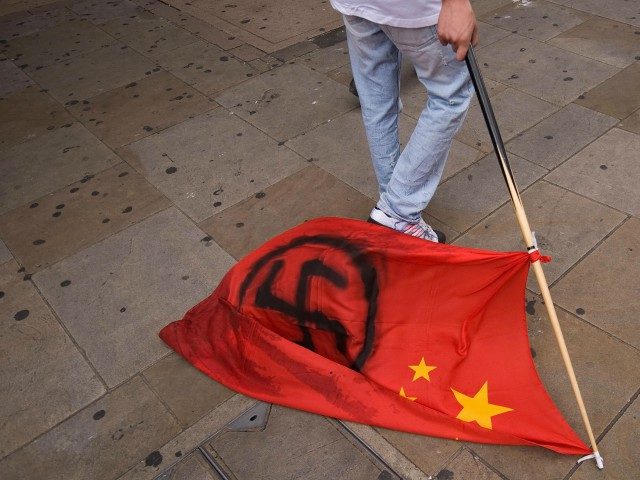 A man drags a Chinese flag daubed with a Nazi swastika along the ground during a protest b