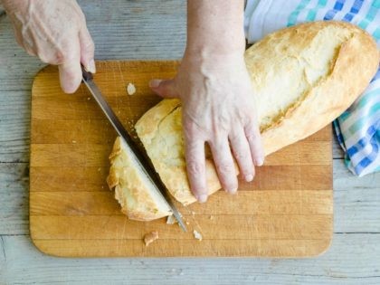 Senior woman cutting freshly baked bread on the wooden board on the rural kitchen table. Traditional bakery concept. Rustic vintage style. Top view.