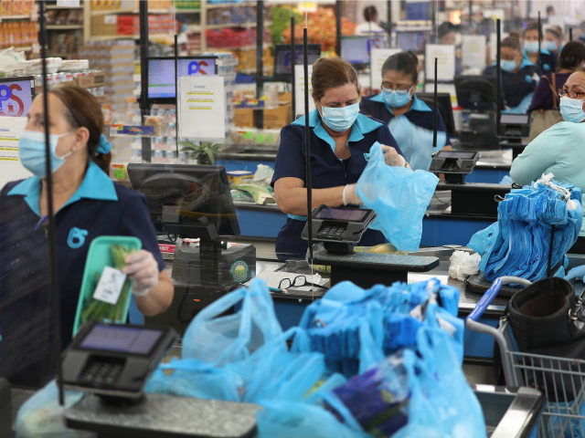 Diana Rivero stands behind a partial protective plastic screen and wears a mask and gloves as she works as a cashier at the Presidente Supermarket on April 13, 2020 in Miami, Florida. The employees at Presidente Supermarket, like the rest of America's grocery store workers, are on the front lines …
