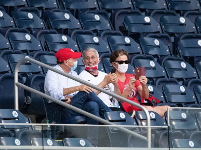 Dr. Anthony Fauci, director of the National Institute of Allergy and Infectious Diseases, center, smiles as he watches an opening day baseball game between the Washington Nationals and the New York Yankees at Nationals Park, Thursday, July 23, 2020, in Washington. (AP Photo/Alex Brandon)