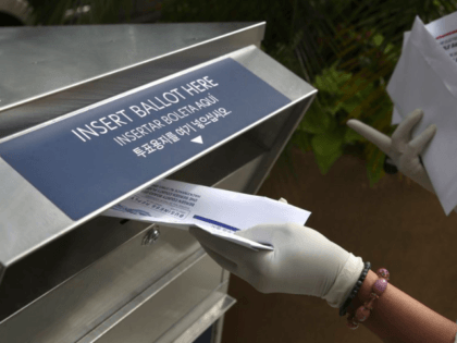 In this July 7, 2020, file photo a woman wearing gloves drops off a mail-in ballot at a drop box in Hackensack, N.J. The November election is coming with a big price tag as America faces the coronavirus pandemic. The demand for mail-in ballots is surging, election workers are in …