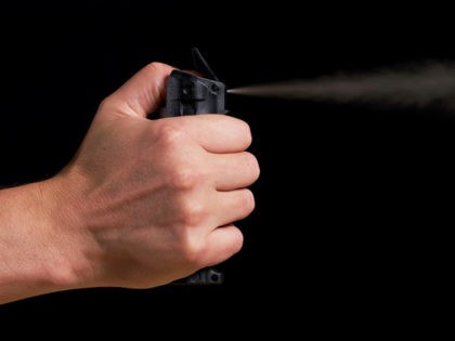 man aiming and spraying pepper spray with visible fog on black background