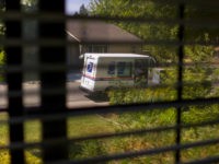 Postal truck and mailman seen through house blinds